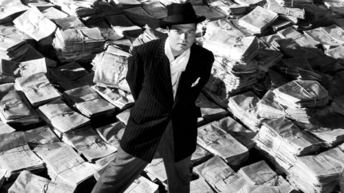 CITIZEN KANE, Orson Welles, 1941, astride stacks of newspaper