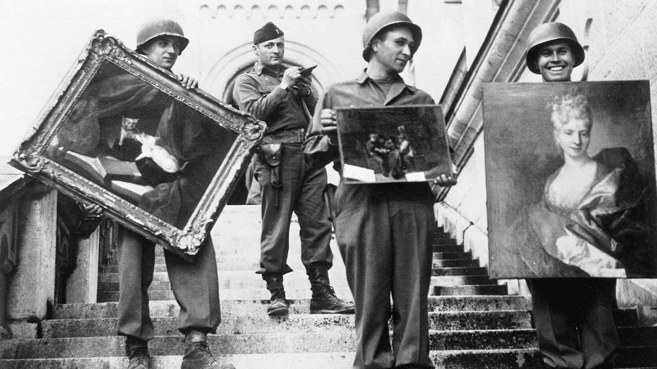 This photo provided by The Monuments Men Foundation for the Preservation of Art of Dallas, shows Monuments Man James Rorimer, with notepad, as he supervises American GI's hand-carrying paintings down the steps of the castle in Neuschwanstein, Germany in May of 1945. From a fairy tale-inspiring castle in the Bavarian Alps to a serene sculpture of Mary and Jesus by Michelangelo tucked away in a church in Belgium, sites and works of art across Europe can give travelers a glimpse at the heroic work done by those who worked to save cultural treasures during World War II.(AP Photo/National Archives and Records Administration)